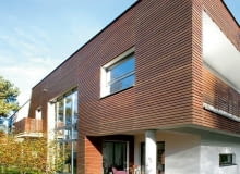 Elewacja ogrodowa. Podcień spełnia funkcję krytego tarasu. W takiej zacisznej, zadaszonej przestrzeni można spędzać czas również w deszczowe dni. Mieszkańcy bardzo sobie cenią to rozwiązanie i latem często z niego korzystają nowoczesny dom, elewacja drewniana, elewacja ogrodowa, taras, słupy