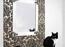 LUSTRO. Często naprawdę niewiele potrzeba, by niemodne i podniszczone przedmioty znów nabrały szyku. Wiszące nad komodą lustro nie miało żadnych mankamentów, w dodatku było bardzo fachowo oprawione. Jednak jego sosnowa rama nie pasowała już do wystroju wnętrza. Teraz ma nowy kolor i dekoracyjne metalowe okucia w narożnikach, dobrane do wzoru zdobiącego tapetę. W efekcie lustro i stojący pod nim mebel wyglądają jak komplet.