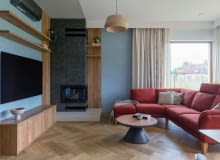 . Obok kominka stanęła duża, rodzinna sofa w bordowym odcieniu oraz stolik łączący drewniane i czarne elementy – zestaw spina całą strefę wypoczynkową.