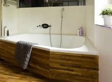 Łazienka, obudowy z drewna. Tekowy parkiet (cena od 209 zł/m kw.) na obudowie i na podłodze sprawia, że duża wanna wtapia się w tło.