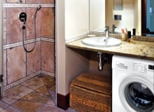 Wnętrza. Kamienny blat z umywalką służy również jako półka na kosmetyki. Inne rzeczy są trzymane w kuferku stojącym obok pralki. Wnętrze oświetla sufitowa lampa z trzema ruchomymi reflektorkami i kinkiety zamontowane na lustrze. Wnętrza. Kamienny blat z umywalką służy również jako półka na kosmetyki. Inne rzeczy są trzymane w kuferku stojącym obok pralki. Wnętrze oświetla sufitowa lampa z trzema ruchomymi reflektorkami i kinkiety zamontowane na lustrze.