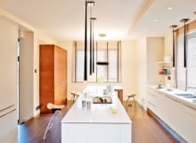 W kuchniach z niską zabudową oświetlenie podszafkowe trzeba zastąpić sufitowym. Modele wybrane do tego wnętrza nie tylko dobrze oświetlają blaty robocze, ale również - ze względu na ciekawą nowoczesną formę - są jego główną ozdobą. Dwa rzędy lamp wiszących, z długimi, przypominającymi sople oprawami z tworzywa sztucznego, zapewniają mocne punktowe oświetlenie miejsc do pracy (na wyspie oraz na blacie pod oknem). Emitowane przez nie światło nie zawsze jest wystarczające w dużej kuchni o powierzchni 28 m kw. Wtedy gospodarze korzystają z halogenów zainstalowanych w częściowo podwieszonym suficie. Oświetlenie wnętrza uzupełnia oryginalna lampa zwieszająca się nad stołem. Fragmenty ścian najbardziej narażone na zabrudzenie obłożono corianem (z tego trwałego i plastycznego materiału są też zrobione blaty).