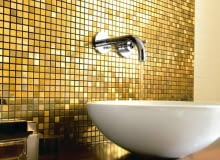 Łazienkę, zwłaszcza w miejscach narażonych na zachlapanie, najczęściej wykańczamy praktycznymi, trwałymi płytkami ceramicznymi - idealnymi do pomieszczeń, w których panuje wilgoć. Można je jednak zastąpić innymi materiałami. Jakimi? Mamy kilka sugestii. <BR /> ŁAZIENKA. Tapeta i szkło. Iście po królewsku: mieniąca się w świetle szklana mozaika w kolo-rze złota doskonale pasuje do dekoracyjnej ramy lustra.