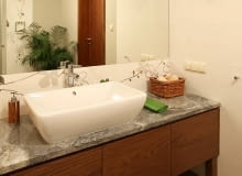 Projektowanie wnętrz. Duże lustro bez ram, kilka różnych źródeł światła (lampa wisząca, halogeny w suficie, kinkiet) - to niezawodne sposoby na optyczne powiększenie wnętrza. Fornirowana orzechem szafka z granitowym blatem stoi na wysokich nóżkach, dzięki czemu wygląda mniej masywnie. LAZIENKA , WNETRZE , OSWIETLENIE