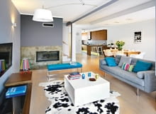 Dom Justyny i Krzysztofa miał być jasny i przestronny. Nowoczesny, ale w żadnym razie nie chłodny. Praktyczny, ale nieprzeładowany przedmiotami. a do tego utrzymany w delikatnych, uspokajających barwach, które łatwo urozmaicić kolorowymi dodatkami. <BR /> WNĘTRZA. Ściany w salonie pomalowano na dwa odcienie szarości. Betonowy fragment wokół kominka pokryto żywicą, stąd ciekawy wzór i kolor. Kąt wypoczynkowy oświetla lampa wisząca, przypominająca nieco przeskalowaną lampę biurkową, oraz zabawna lampka-łowiczanka, autorstwa polskiej projektantki Katarzyny Herman-Janiec.