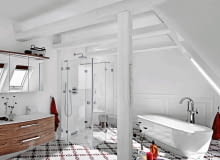 <B> Monotonia bywa męcząca - nie tylko w życiu, ale także w mieszkaniu. Na przykład łazienka zaaranżowana w neutralnych barwach będzie wprawdzie zawsze na czasie, ale łatwo się może znudzić. Dlatego radzimy: wprowadź akcent w mocnym kolorze. Nawet pojedynczy potrafi zdziałać cuda. </B><BR /> Głównym akcentem kolorystycznym w białej łazience, a właściwie komfortowym pokoju kąpielowym, są położone na podłodze płytki ceramiczne z graficzno-kwiatowym wzorem w dwóch mocnych barwach: czerwieni i granatu. Pomieszczenie znajduje się na poddaszu, stąd skośne ściany, belki stropowe i słup konstrukcyjny. Drewniane elementy architektoniczne często pozostawia się w naturalnym kolorze, by dodać wnętrzu przytulności i podkreślić jego strychowy charakter. Tutaj zdecydowano się je pomalować na kolor ścian i sufitu, przez co wnętrze wydaje się jeszcze większe. Białe są również łazienkowe urządzenia o prostych formach, które wtapiają się w tło i nie rzucają się w oczy. <B> Monotonia bywa męcząca - nie tylko w życiu, ale także w mieszkaniu. Na przykład łazienka zaaranżowana w neutralnych barwach będzie wprawdzie zawsze na czasie, ale łatwo się może znudzić. Dlatego radzimy: wprowadź akcent w mocnym kolorze. Nawet pojedynczy potrafi zdziałać cuda. </B><BR /> Głównym akcentem kolorystycznym w białej łazience, a właściwie komfortowym pokoju kąpielowym, są położone na podłodze płytki ceramiczne z graficzno-kwiatowym wzorem w dwóch mocnych barwach: czerwieni i granatu. Pomieszczenie znajduje się na poddaszu, stąd skośne ściany, belki stropowe i słup konstrukcyjny. Drewniane elementy architektoniczne często pozostawia się w naturalnym kolorze, by dodać wnętrzu przytulności i podkreślić jego strychowy charakter. Tutaj zdecydowano się je pomalować na kolor ścian i sufitu, przez co wnętrze wydaje się jeszcze większe. Białe są również łazienkowe urządzenia o prostych formach, które wtapiają się w tło i nie rzucają się w oczy.