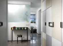 Oryginalny front szafy w przedpokoju tworzą prostokąty z lakierowanej płyty MDF w odcieniach szarości, beżu i bieli. Wnętrze rozświetla naturalne światło wpadające przez mleczną szybę, za którą znajduje się kuchnia. UWAGA PONOWNA PUBLIKACJA ZA ZGODA WLASCICIELI