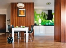 Za dnia mieszkanie jest rozjaśnione światłem, które wpada przez okno balkonowe i odbija się od lustra zamontowanego na ścianie pokoju dziennego. Wieczorem to ogromne lustro zwielokrotnia z kolei światło lamp. Projektantki oraz gospodarze - Małgorzata i Sebastian - zgodnie uznali, że w tym wnętrzu nastrój będzie budowało oświetlenie. <BR /> MIESZKANIE. Fragment kuchni jest?widoczny z części dziennej, dlatego zastosowano w niej eleganckie materiały: szafki są z lakierowanej na biało płyty MDF, blat z czarnego granitu. Ścianę nad nim wyklejono fototapetą z motywem konwalii i przykryto szkłem. Reprodukcja w ramce nad stołem to tak naprawdę... nowoczesny klimatyzator. kuchnia, wystrój wnętrz, meble kuchenne