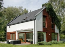 BIel, antracyt i drewno egzotyczne - pięknie ze sobą skontrastowane - tworzą atrakcyjne tło dla pnączy porastających dom od północnej strony. Cienkowarstwowemu tynkowi strukturalnemu towarzyszą na elewacjach drewno modrzewiowe oraz ciemna dachówka duże okna, projekty domów