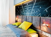 SYPIALNIA. Fototapeta, przedstawiająca surową stalową konstrukcję w opuszczonej hali fabrycznej, to po łóżku drugi element wystroju nawiązujący do klimatu loftowego. Kontrastem dla niej jest zagłówek z miękkich poduch obitych tkaniną przypominającą welur. Na podłodze ułożono dębowe deski, lekko pobielane. Pasuje do nich surowe drewno, z którego zrobiono łóżko. Gdy podstawa łóżka jest szersza od materaca, nie potrzeba już stolików nocnych. Niezbędne drobiazgi można postawić na brzegu mebla.