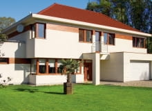 Elewacja: jasny tynk z fragmentami obłożonymi drewnem; Dach: czerwony, zbliżony do koloru drewna; Okna i drzwi: profile i skrzydła zbliżone do barwy drewna; Brama garażowa: biała, dopasowana do barwy tynku elewacyjnego