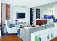 ZA KANAPĄ stanął niski regalik, w sam raz na czytane właśnie książki i dekoracyjne drobiazgi. Na granicy salonu i kuchni uwagę zwraca nietypowa półka na wino, zaprojektowana na wymiar i zrobiona przez stolarza.