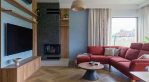 . Obok kominka stanęła duża, rodzinna sofa w bordowym odcieniu oraz stolik łączący drewniane i czarne elementy – zestaw spina całą strefę wypoczynkową.