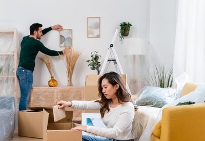 Zwei Personen packen Umzugskartons in einem Wohnraum aus.