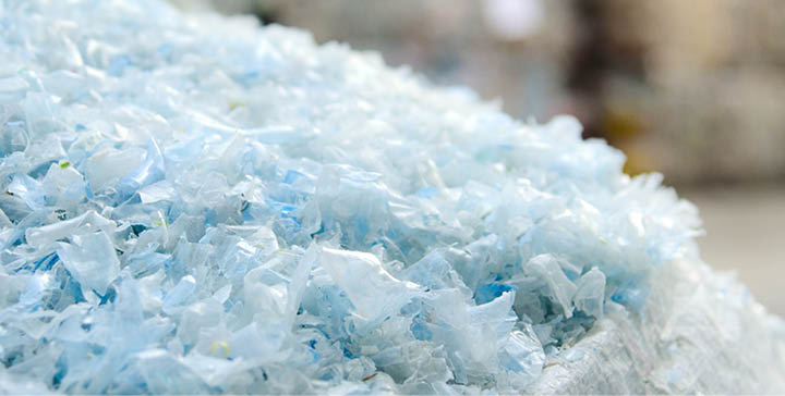 Close up PET plastic bottle flakes in white big bag with blur plastic bottle bales background