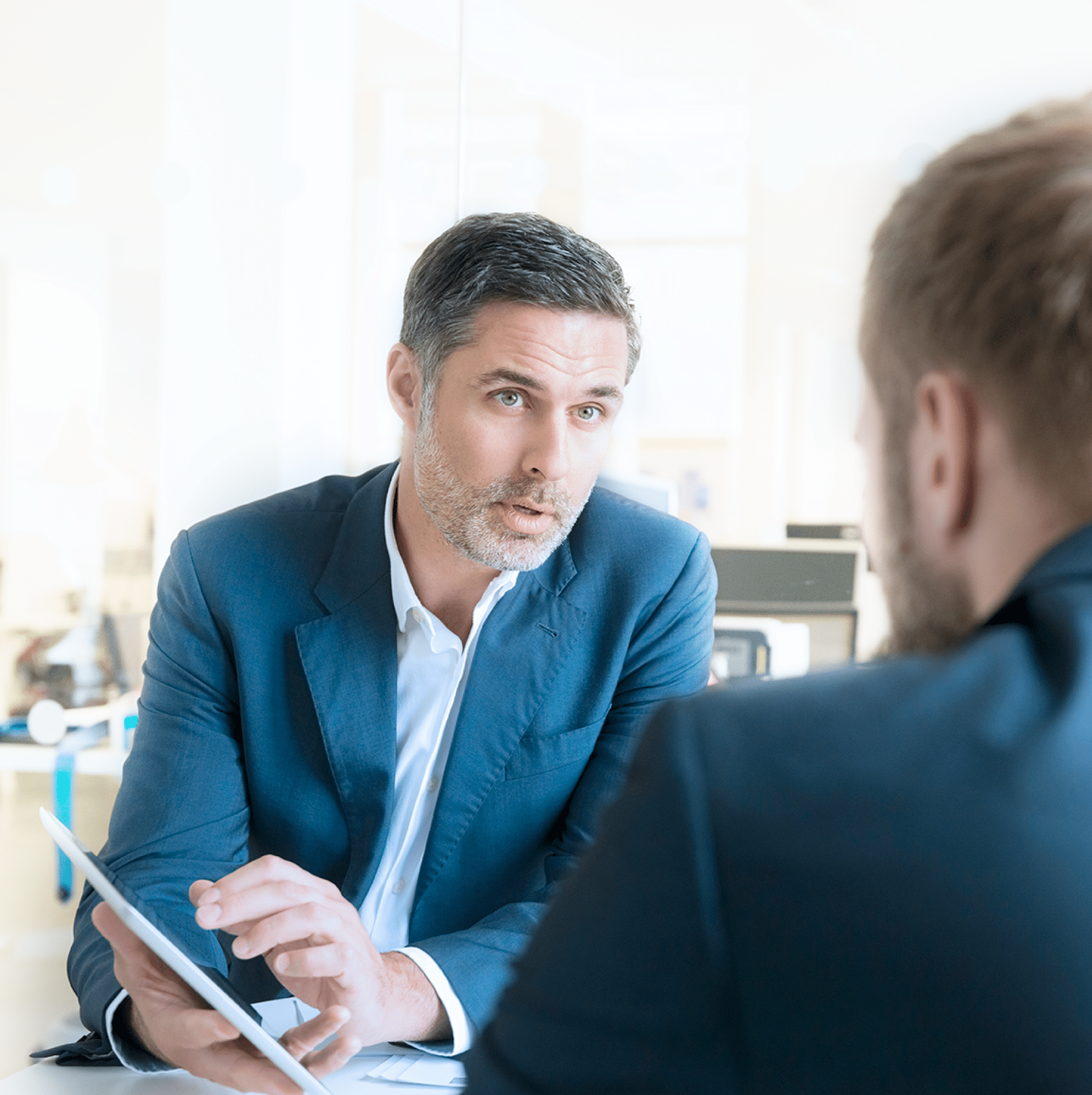 Businessman discussing over digital tablet with male colleague at desk in office