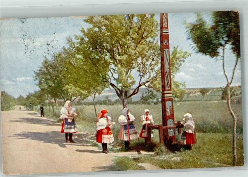 1912 sign. Sukaneho Mädchen in Tracht an einer Säule am Rande einer Straße