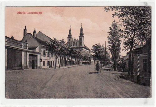 AK von Maria Lanzendorf. Straßenpartie mit Kirche gelaufen. Leichter Bug oben links mitte und rechts, unten rechts, kleiner Knick unten rechts und mitte, leichte bräunliche FlEcke n auf der Vorder- und Rückseite, sonst gut erhalten.