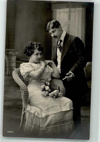 Eleganter Mann mit Zigarette redet auf eine im Sessel sitzende Frau mit Rosen ein