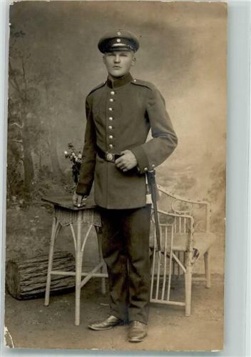 Ein junger Landser in Uniform mit Portepee und Schirmmütze im Fotostudio