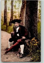 Junger Mann mit Schirm und Pfeife im Wald sitzend