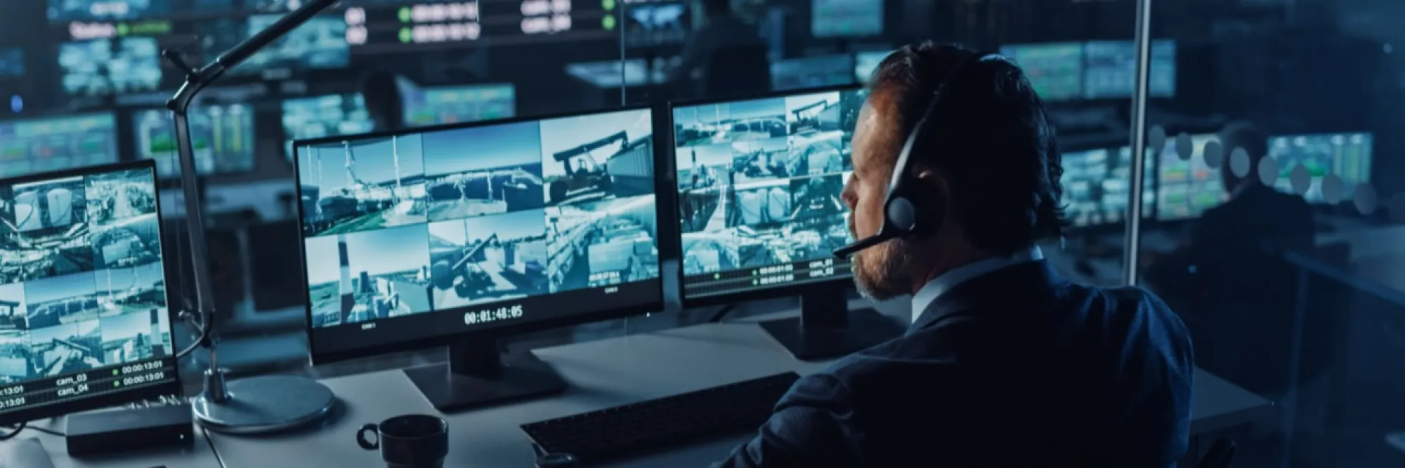 Male Officer Works on a Computer with Surveillance CCTV Video in a Harbour Monitoring Center with Multiple Cameras on a Big Digital Screen