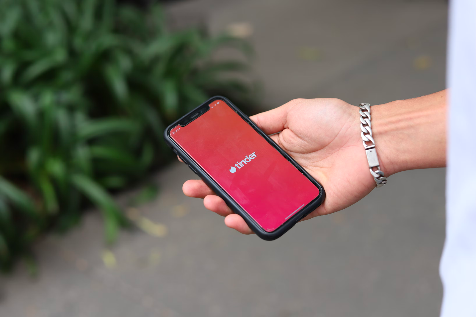 Eine Hand hält ein iPhone, auf dem die Tinder-App geöffnet ist.