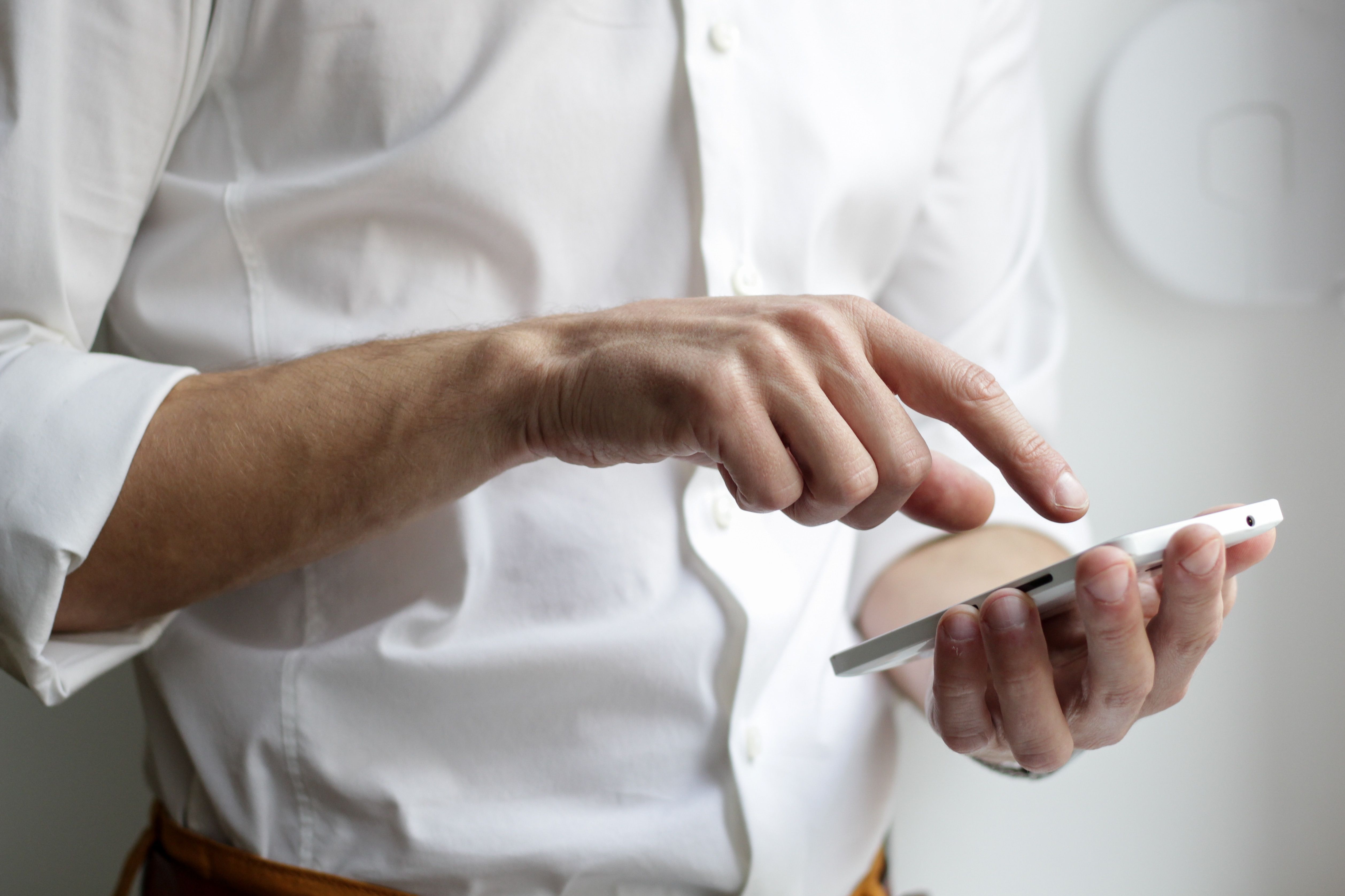 Mann im weißen Hemd hält ein Smartphone in der Hand und sucht online nach Tipps, was er tun kann, wenn er Opfer von Online-Betrug geworden ist.