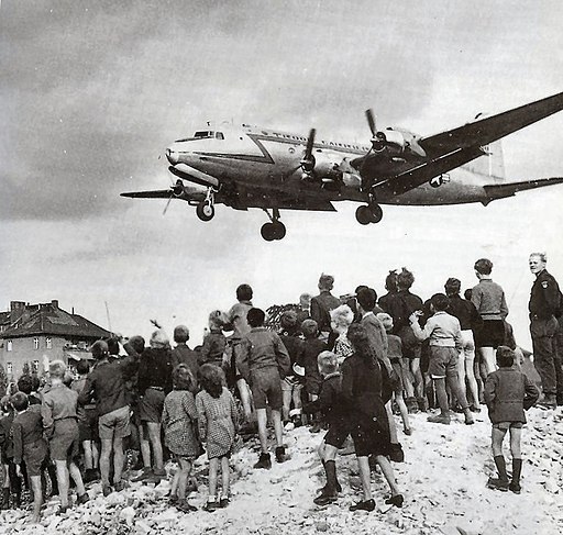 Pont aérien de Berlin Des enfants regardent un avion arriver pendant le pont aérien de Berlin StudySmarter