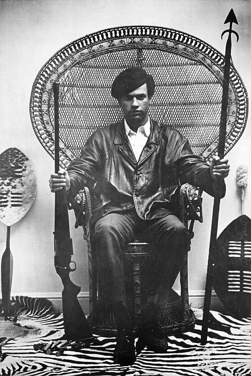 Black Power Movement Huey Newton portrait with a gun in a rattan chair StudySmarter