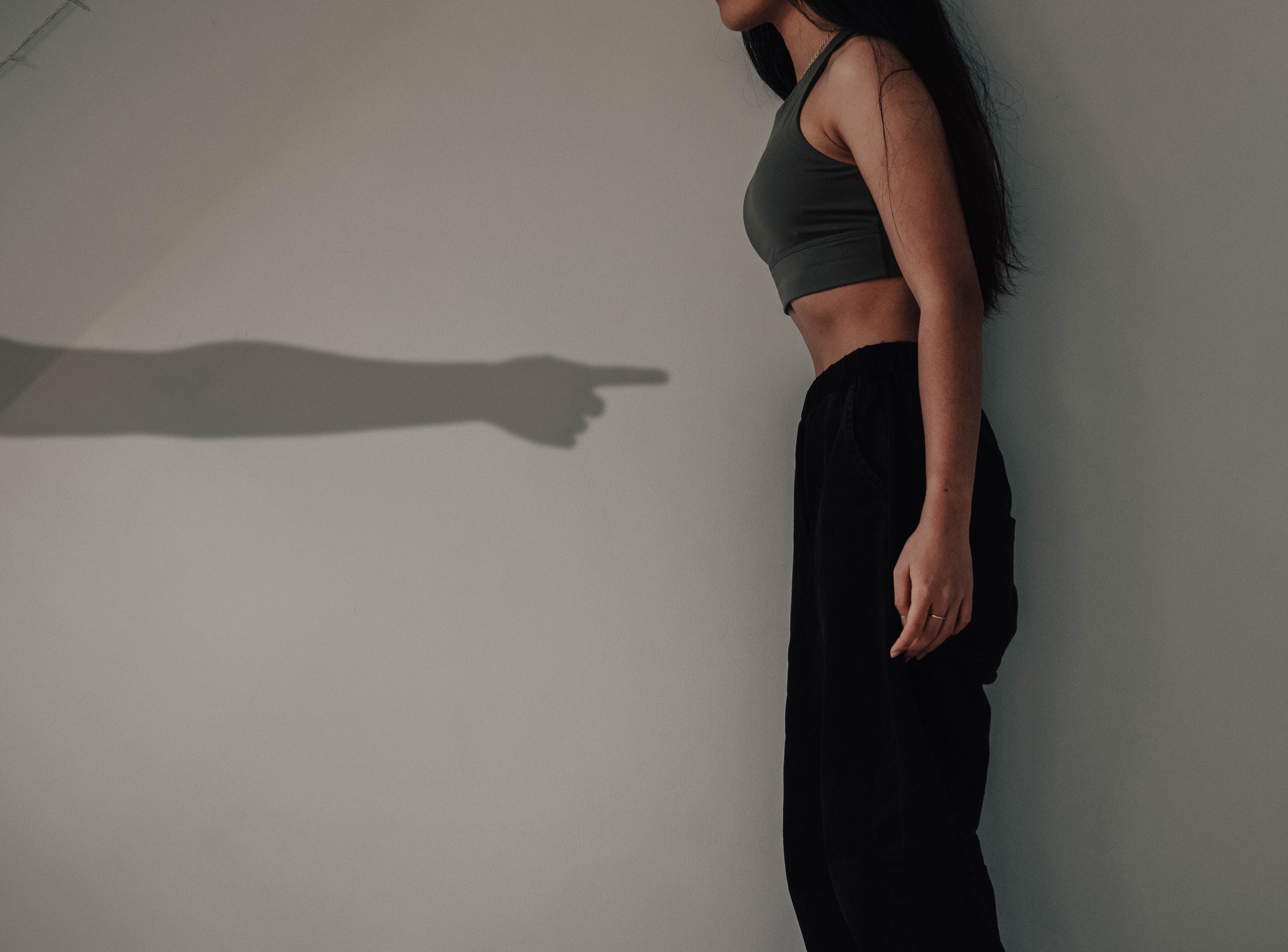 Social Learning Theory Anorexia, image of a woman sucking in stomach and a shadow of a hand pointing at her stomach, StudySmarter
