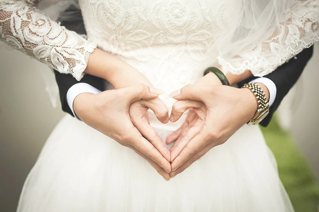 Social Development in Adulthood, a bride and groom making a heart shape with their hands, StudySmarter