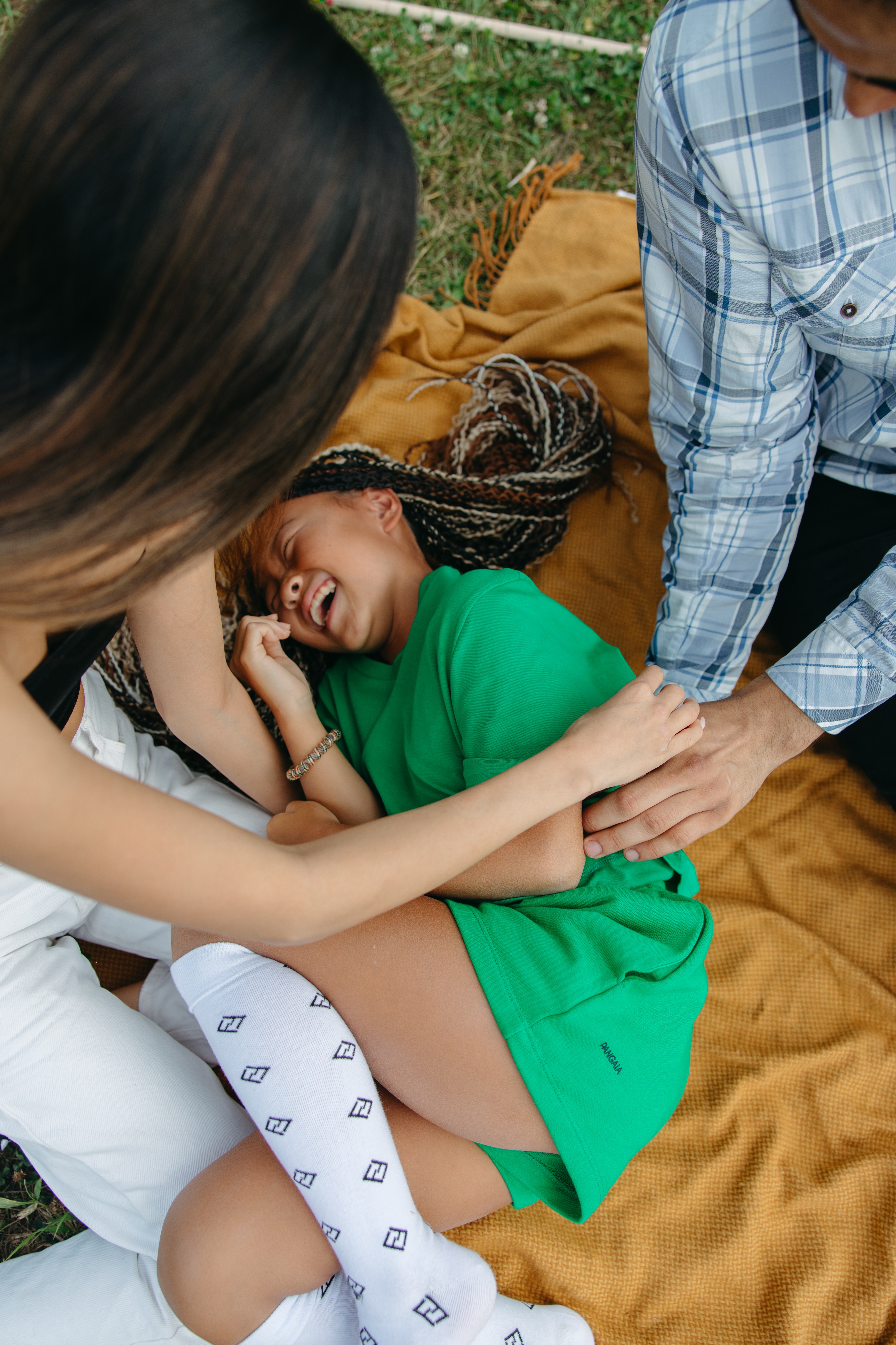 Sentidos de la piel, Foto de una niña a la que dos adultos le hacen cosquillas tumbada en una manta sobre la hierba, StudySmarter