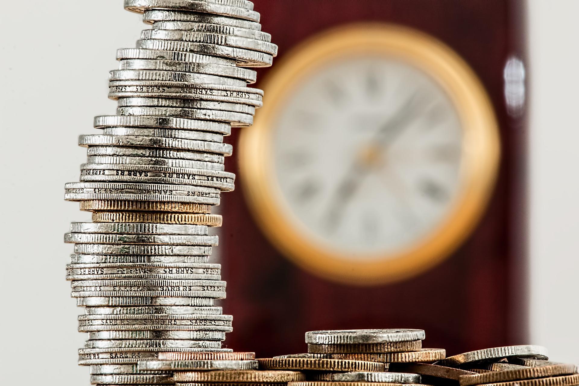 Defining and Measuring Social Class, Coins stacked up on each other with a blurred clock in the background, StudySmarter