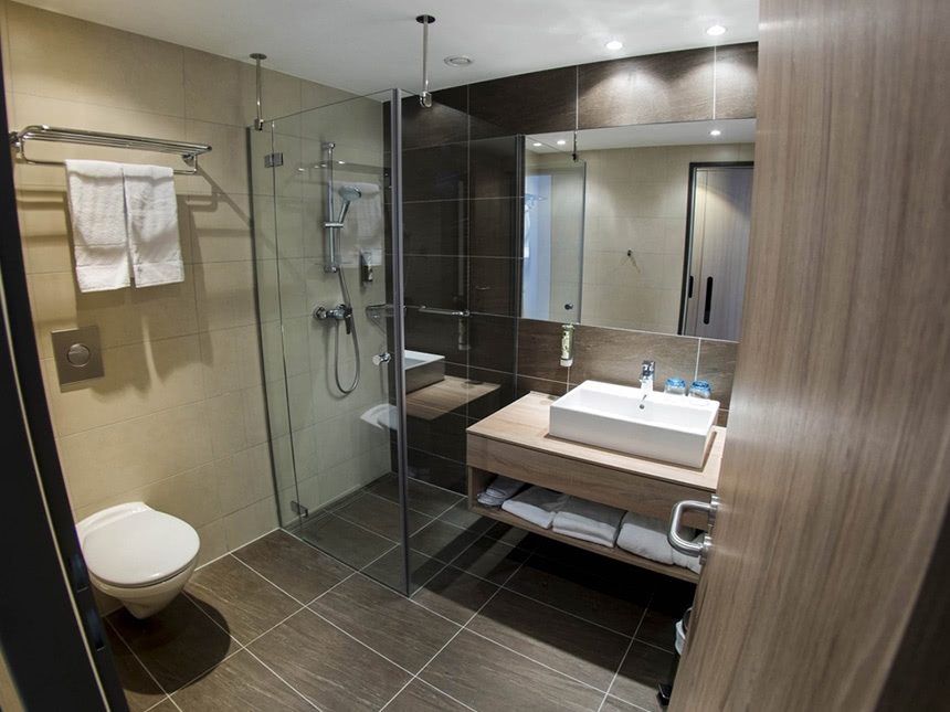 Badbereich mit Dusche, WC, Waschtisch und großen Wandspiegel