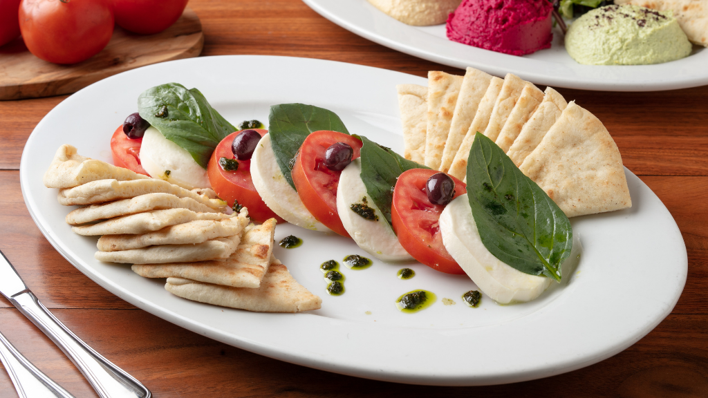 Caprese Appetizer: Thickly sliced buffalo mozzarella topped with roma tomatoes, fresh basil, kalamata olives, & homemade pesto