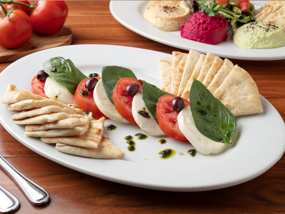 Caprese Appetizer: Thickly sliced buffalo mozzarella topped with roma tomatoes, fresh basil, kalamata olives, & homemade pesto