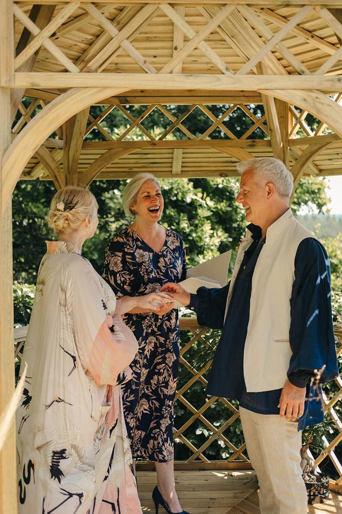 Sara Price Celebrant laughing with groom as bride looks on during a vow renewal ceremony in a garden pagoda