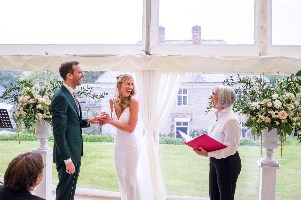 Sara Price Celebrant and bride sharing a laugh during the ring exchange in a wedding ceremony in a marquee in the garden.