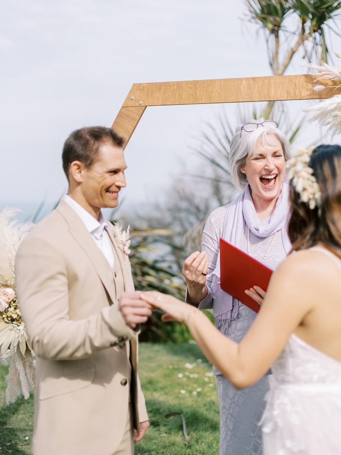 Sara Price Celebrant laughing with bride as groom looks on during a wedding ceremony in a hotel garden by the sea