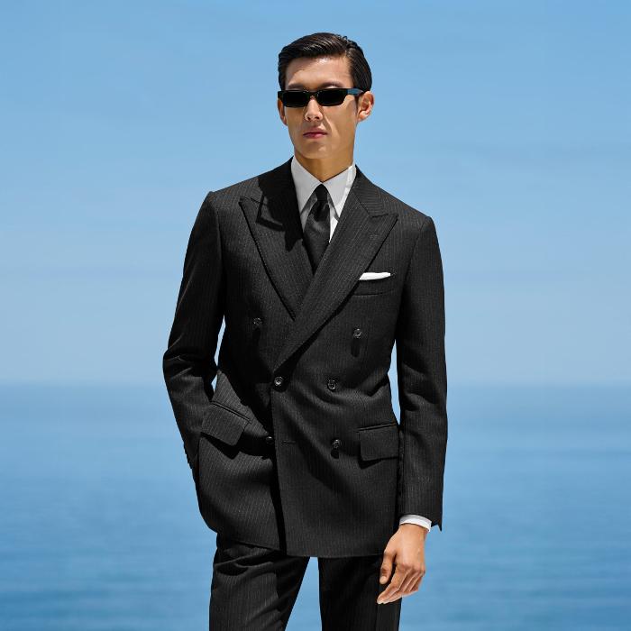 This black striped suit is cut to a tailored fit, offering a refined silhouette with structured shoulders. Paired with slim trousers featuring side-adjusters and a flat front for modern sophistication.