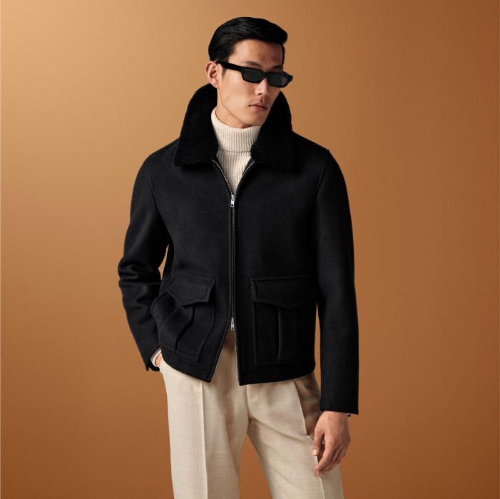 This black bomber jacket hits at the hip and includes a detachable shearling collar, double-ended zip, and box pleat pockets. Lined with inside pockets for added utility.