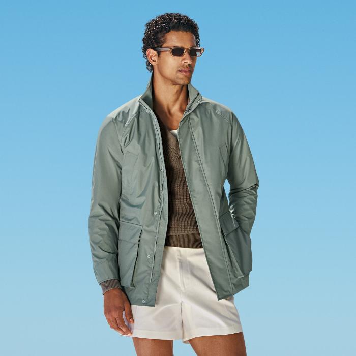 Mid green field jacket with raglan shoulders and a sleek hip-length cut. Features hidden snap buttons, zip closure, and an interior waist drawstring. Includes flapped and slanted pockets.