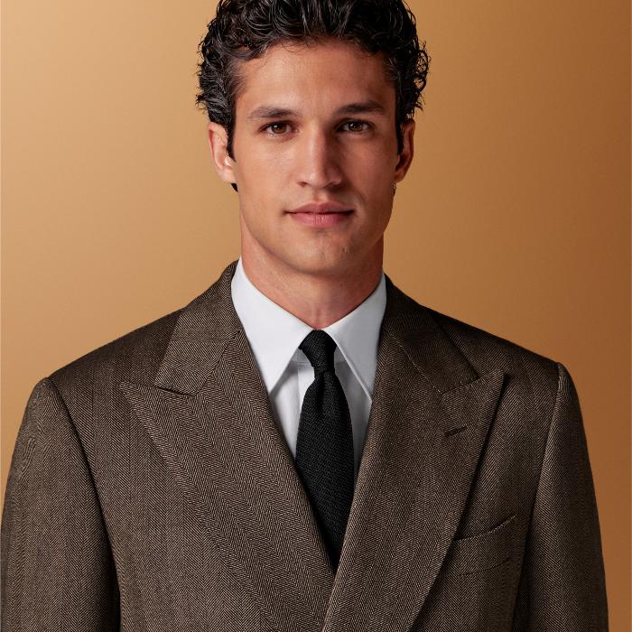 This mid brown herringbone suit is cut to a tailored fit with a padded shoulder and fitted silhouette. Paired with wide-leg straight trousers featuring a single pleat and belt loops.