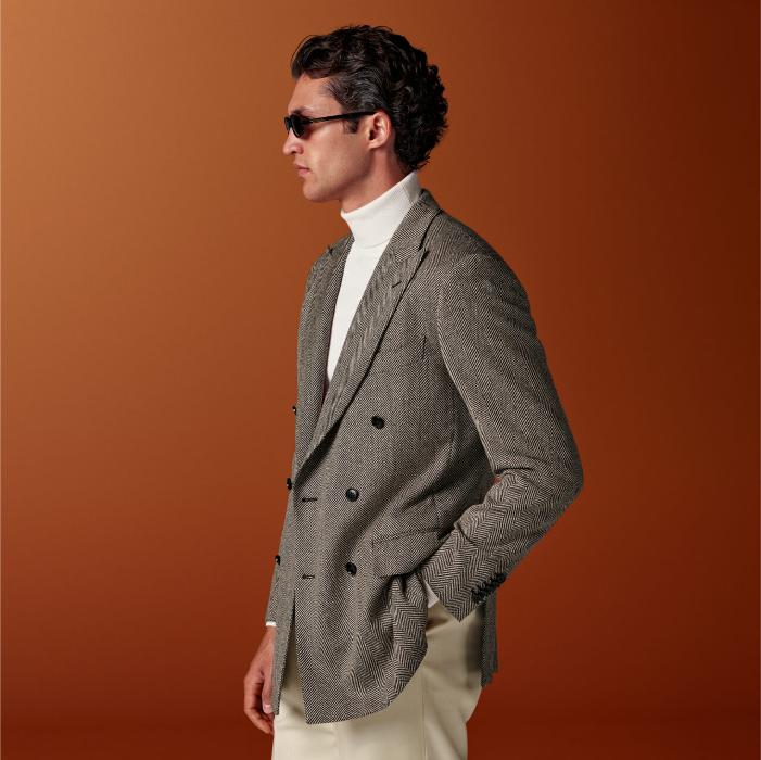 This brown herringbone blazer is cut to a tailored fit with a slim chest and waist for a fitted silhouette and features a padded shoulder, double-breasted closure, and peak lapels.
