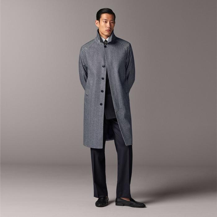 Navy herringbone overcoat with relaxed raglan sleeves. Features knee-length cut, single-breasted hidden buttons, button welted pockets, inside pockets, sleeve straps, back inverted box pleat, and single vent. Lined for comfort.