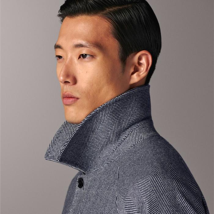 Navy herringbone overcoat with relaxed raglan sleeves. Features knee-length cut, single-breasted hidden buttons, button welted pockets, inside pockets, sleeve straps, back inverted box pleat, and single vent. Lined for comfort.