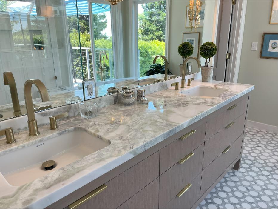 A striking countertop anchors this bathroom remodel, paired with custom cabinetry, dual sinks, and decorative lighting. Stone finishes and modern detailing elevate this vanity area, showcasing functional elegance within a timeless bathroom design.