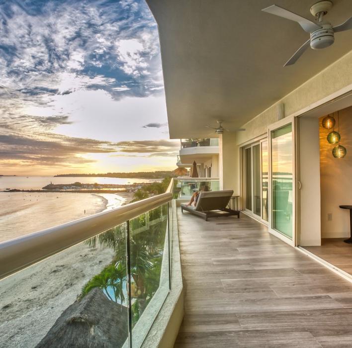 An expansive seaside patio with panoramic ocean views creates a serene extension of living space. Wide-plank flooring and sleek glass railings frame the horizon, offering a modern retreat ideal for second homes and beach house remodels.