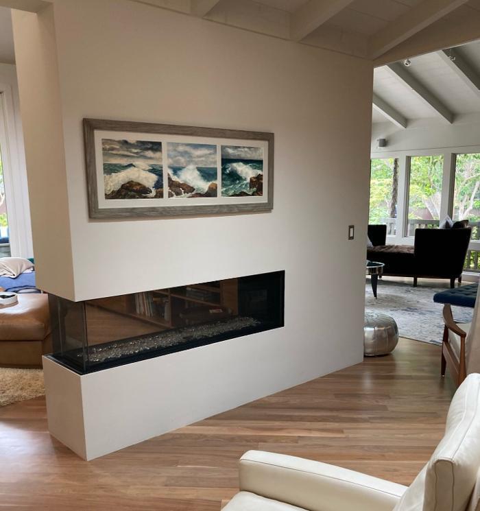 A modern three-sided fireplace creates a seamless transition between living spaces, complemented by diagonally installed walnut floors for warmth and architectural rhythm.